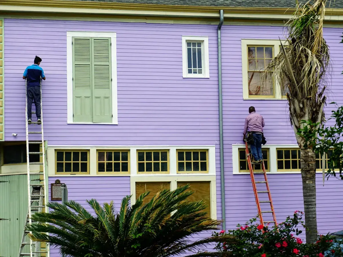 Zwei Maler streichen von Leitern aus die Fassade eines Wohnhauses