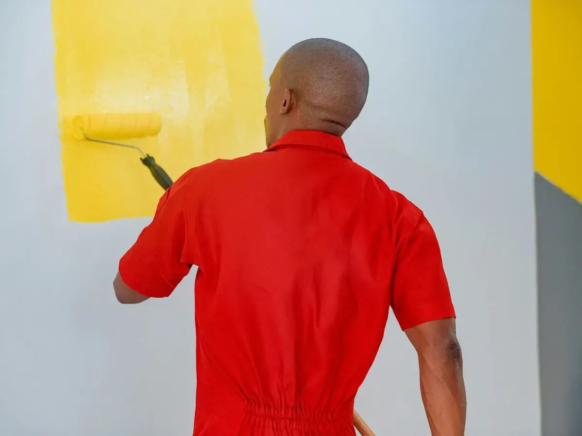 Maler trägt mit der Rolle gelbe Farbe auf eine Wand auf
